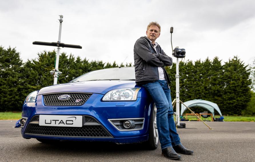 U.K. Secretary of State for Transport Grant Shapps sitting on blue car on test track