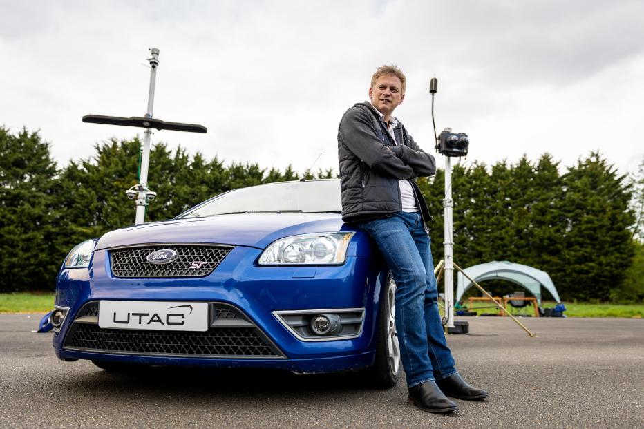 U.K. Secretary of State for Transport Grant Shapps sitting on blue car on test track