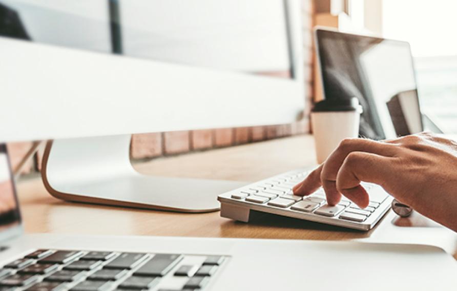 Man typing at a desktop Mac computer with a laptop and IPad nearby